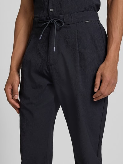 Männermodel trägt Stoffhose mit elastischem Bund von Closed, dunkler Material-Mix mit Stretch-Anteil, Strukturmuster, Eingrifftaschen, Nahaufnahme Oberkörper.