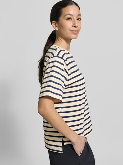 Modelka kobieca nosi Regular Fit T-Shirt aus reiner Baumwolle Modell 'MULTID' od Weekend Max Mara, prążkowana bawełna, kremowo-granatowe paski, krótki rękaw, asymetryczny dół z rozcięciami po bokach, nadruk z logo, widok boczny, ujęcie górnej części ciała.