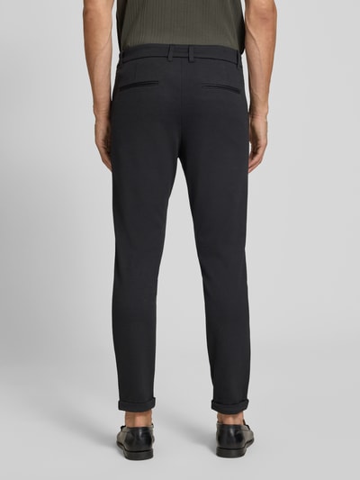 Męski model nosi Slim Fit Hose mit Viskose-Anteil in verkürzter Passform von Lindbergh, czarne, mieszanka wiskozy, kieszenie z tyłu, krój slim fit, szerokość w rozmiarze M: 42 cm, długość wewnętrzna nogawki: 72 cm, materiał elastyczny, widok całej sylwetki od tyłu.