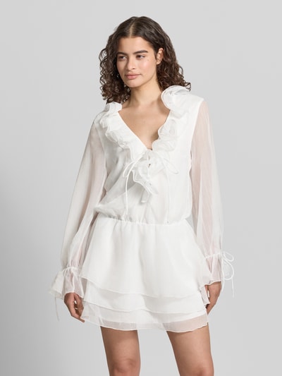 Vrouwenmodel draagt Minikleid met Rüschen und V-Ausschnitt van Gina Tricot in wit, getailleerd model, mouwen met vetersluiting, ganzkörperansicht van voren, ruglengte maat XS 85 cm, borstwijdte maat XS 49 cm, mouwlengte maat XS 64 cm