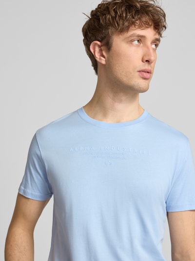 Männermodel trägt T-shirt mit labelprint und ronde hals van Alpha Industries uit puur katoen, regular fit, ruglengte maat M 67 cm, nahaufnahme bovenlichaam.