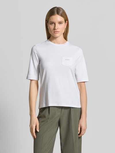 Frauenmodel trägt Regular Fit T-Shirt mit Brusttasche Modell 'Tonja' von JOOP!, reine Baumwolle, weiß, Logo-Detail, Rundhalsausschnitt, Ganzkörperansicht von vorne.