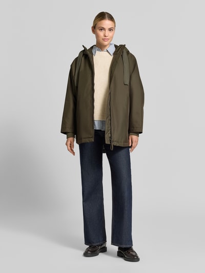 Frauenmodel trägt Relaxed Fit Mantel mit Kapuze Modell 'PURE' von g-lab, olivgrün, Tunnelzug, Eingrifftaschen, Ganzkörperansicht von vorne. Rückenlänge 69 cm, Schulterbreite 45 cm, Brustweite 88 cm, Ärmellänge 60 cm.