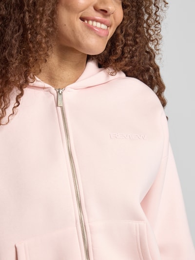 Kobiece modelka nosi Relaxed Fit Sweatjacke mit Kapuze od REVIEW z czystej bawełny, logo, kieszenie kangurki, krój relaxed fit, zbliżenie na górną część ciała.