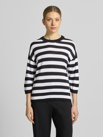 Frauenmodel trägt Regular Fit Oberteil aus Viskose-Mix Modell 'Lani' von GUIDO MARIA KRETSCHMER WOMAN, Strick-Optik, 3/4-Arm, Rundhalsausschnitt, elastische Ärmelabschlüsse, schwarz-weiße Streifen, glatte Textur, Ganzkörperansicht von vorne.