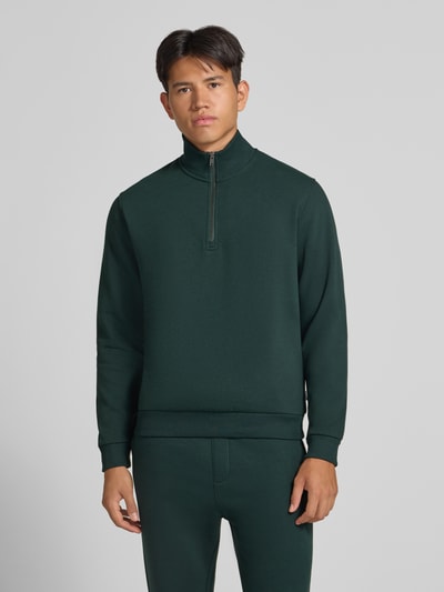 Männermodel trägt Regular Fit Sweatshirt mit Baumwoll-Anteil Modell 'Bradley' von JACK & JONES in Dunkelgrün, glatte Textur, Troyer-Kragen, Ganzkörperansicht von vorne, Rückenlänge 68 cm, Ärmellänge 66 cm.