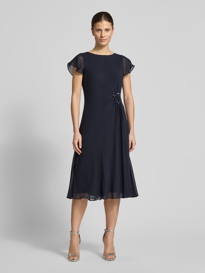Frauenmodel trägt knielanges Cocktailkleid mit Ziersteinbesatz von Christian Berg Cocktail in Dunkelblau, Chiffon, tailliert, Ganzkörperansicht von vorne.