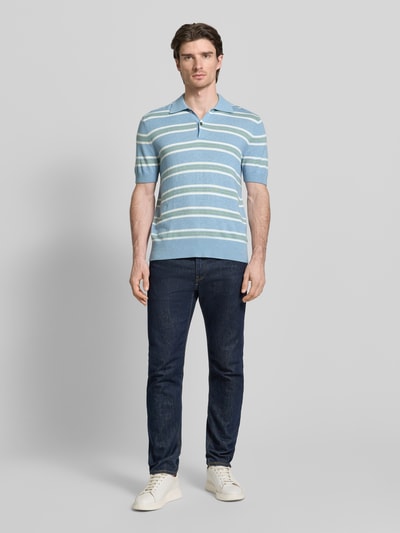 Männermodel trägt Poloshirt aus Baumwoll-Lyocell-Mix mit Kaschmir-Anteil von FTC-Cashmere, Hellblau mit weißen Streifen, Regular Fit, gerippte Abschlüsse, Polokragen, kurze Knopfleiste, hochwertige Textur, Ganzkörperansicht von vorne.