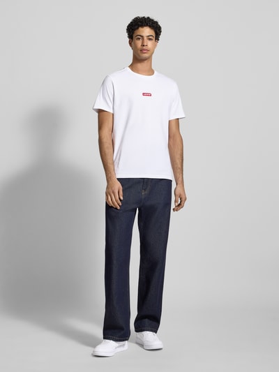Männermodel trägt T-Shirt mit Label-Detail von Levi's®, weiße Baumwolle, Relaxed-Fit, gerippter Rundhalsausschnitt, Ganzkörperansicht von vorne. Rückenlänge bei Größe M: 70 cm.