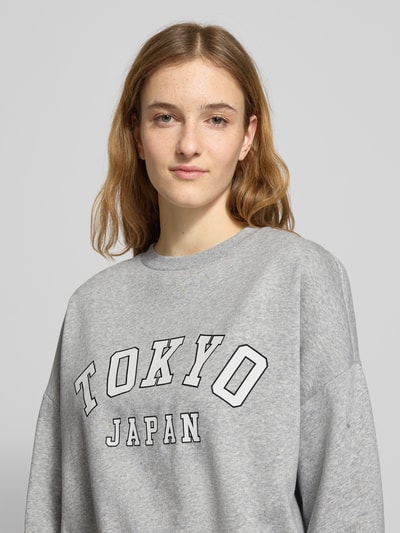 Modelka kobieca nosi szary Oversized Sweatshirt aus Baumwoll-Mix Modell 'SWEAT LIFE' od Only z nadrukiem, okrągły dekolt, tekstura sweat, zbliżenie na górną część ciała.