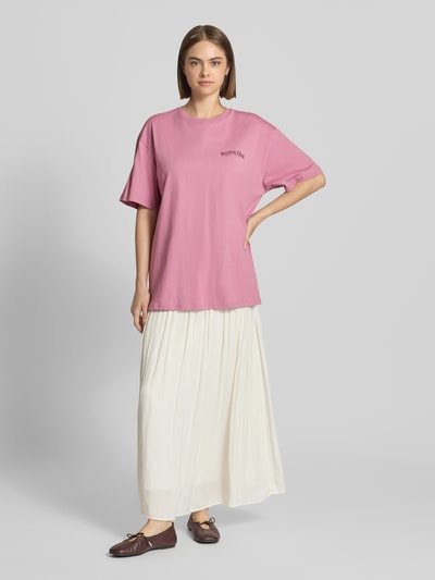 Frauenmodel trägt Oversized Fit T-Shirt aus reiner Baumwolle mit Label-Detail von REVIEW in Rosa zu weißem Rock, Damen T-Shirt, Ganzkörperansicht von vorne.