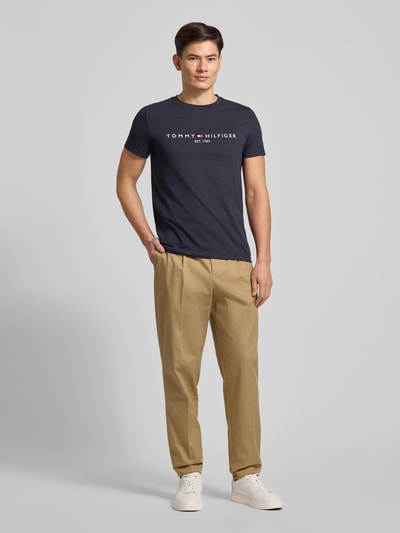 Männermodel trägt T-Shirt aus Bio-Baumwolle von Tommy Hilfiger in Dunkelblau mit Logo-Stickerei, gerader Schnitt, Rundhalsausschnitt, Ganzkörperansicht von vorne.