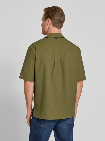 Männermodel trägt Relaxed Fit Freizeithemd aus Seersucker-Material von Tommy Hilfiger, Optik:Allover-Muster, Kellerfalte, Ärmelform: Kurzarm, Materialverarbeitung: Seersucker, grün mit feiner Struktur, Ganzkörperansicht Rückansicht.
