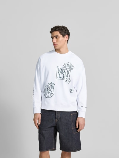 Männermodel trägt Oversized Sweatshirt aus Baumwoll-Mix von MAISON KITSUNÉ in Weiß mit floralen Label-Stitchings, Ganzkörperansicht von vorne.