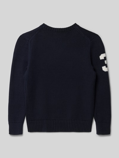 Junge trägt Strickpullover mit Motiv und Rundhalsausschnitt von Polo Ralph Lauren Teens in Dunkelblau, Reine Baumwolle, Regular-Fit, Rückenlänge bei Größe S 49 cm, Ärmellänge 47 cm, Motiv weiße 3 auf dem Ärmel, Ganzkörperansicht Rückansicht.