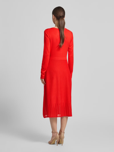 Modelka kobieta ma na sobie Tailliertes Strickkleid aus Viskose-Mix od s.Oliver BLACK LABEL, kolor czerwony, długość midi, faktura plisowana, dopasowany krój, rękawy długie, okrągły dekolt, drobny dzianinowy splot, widok całej sylwetki z tyłu.