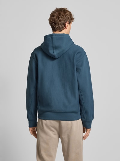 Męski model trägt Hoodie mit Kapuze von Carhartt Work In Progress, mieszanka bawełny, luźny krój, kaptur, tunel, wyhaftowane logo, kieszeń kangurka, prążkowane wykończenia, kolor niebieski i beżowy, długość tyłu 70 cm, długość rękawów 64 cm, całe ciało z tyłu.
