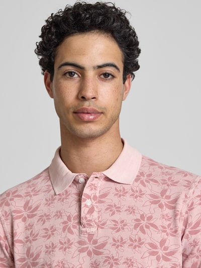 Männermodel trägt Slim Fit Poloshirt mit kurzer Knopfleiste Modell 'FRISCO' von Blend, rosa mit floralem Muster, reine Baumwolle, Nahaufnahme Oberkörper.