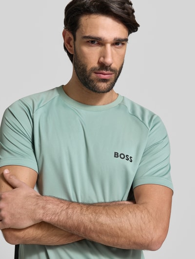 Mężczyzna nosi Slim Fit T-Shirt mit Label Print Modell 'TOP SPIN CB' od BOSS Green, kolor jednolity, krótki rękaw, dekolt okrągły, subtelna faktura materiału. Nahaufnahme Oberkörper.