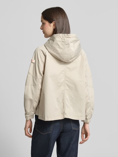 Młody modelka nosi kurtkę Jacke mit Zweiwege-Reißverschluss Modell 'DOLORES NEO' von Frieda & Freddies z mieszanki bawełny, prosty krój, kaptur z ściągaczem, naszywka z logo, kieszenie z patką, elastyczne zakończenia rękawów, regulowany dół, kremowy kolor, długość tyłu 59 cm, szerokość ramion 48 cm, szerokość w rozmiarze 36: 50 cm, długość rękawów 52 cm, widok całej sylwetki od tyłu.
