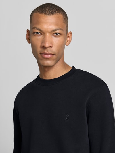 Mężczyzna nosi bluzę Regular Fit Sweatshirt aus reiner Baumwolle model 'BAARO' od ARMEDANGELS, czarny kolor, gładka tekstura, zbliżenie na górną część ciała.