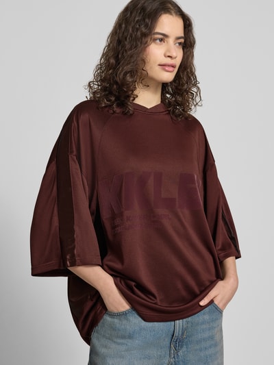 Kobieta prezentuje Oversized T-Shirt mit Label-Print von Karo Kauer, damski t-shirt, krój oversized, nadruk z logo, dekolt w serek, długość tyłu w rozmiarze S: 71 cm, przód, ujęcie całej sylwetki