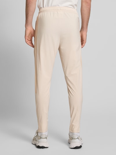 Męski model nosi Jogpants mit elastischem Bund od adidas Sportswear, jasny beż, prosty krój, elastyczny pas, widok całej sylwetki z tyłu.
