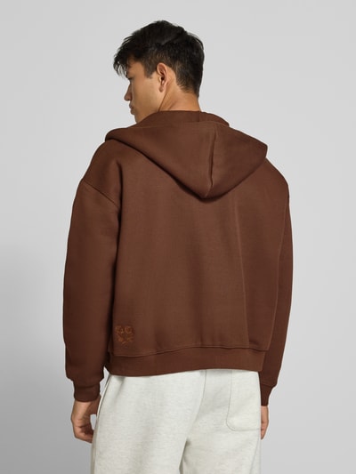 Männermodel trägt braune Sweatjacke mit Kapuze von ANOTHER COTTON LAB, lockerer Schnitt, Baumwoll-Mix, Rückansicht Ganzkörperansicht.