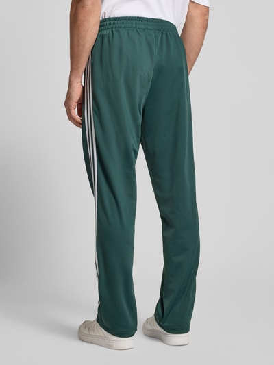 Männermodel trägt Sweatpants mit elastischem Bund von adidas Originals, Dunkelgrün mit weißen Streifen, Eingrifftaschen, Label-Stitching, Lockerer-Schnitt, Ganzkörperansicht Rückansicht.