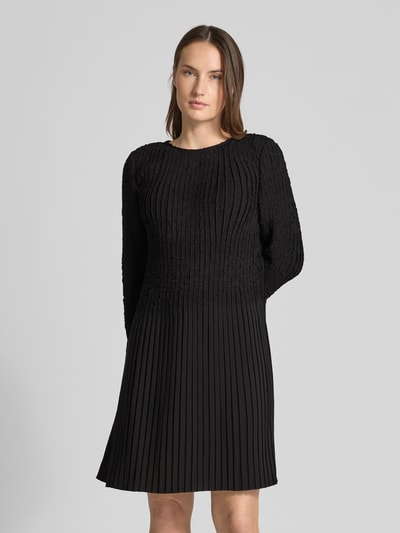 Vrouwenmodel draagt Tailliertes Cocktailkleid mit Raffung-Optik Modell 'Doppar' van BOSS in zwart, getailleerde fit, mini lengte, ronde hals, gestructureerd motief, lange mouwen met frill manchetten, unicolor, ruches details, frill zoom, keyhole rug, volledige lichaamsweergave van voren.