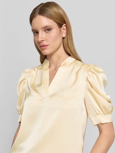Frauenmodel trägt Blusenshirt mit Puffärmeln Modell 'Roella' von Neo Noir aus Satin in hellem Beige, gerader Schnitt, Serafino-Kragen, Nahaufnahme Oberkörper.