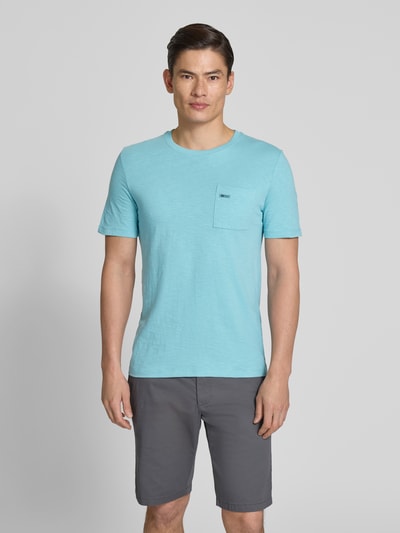 Męski model nosi Regular Fit T-Shirt aus reiner Baumwolle od s.Oliver RED LABEL, jasnoniebieski kolor, gładka faktura, mała kieszonka, krótki rękaw, krój regular fit, bawełna, widok całej sylwetki z przodu.