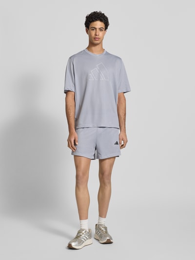 Männermodel trägt Shorts mit Label-Print von adidas Training in Hellgrau, Lockerer-Schnitt, Elastischer-Bund, Ganzkörperansicht von vorne.