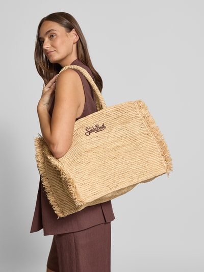 Vrouwenmodel draagt Shopper met Label-Stitching model 'VANITY RAFFIA FRINGES' van MC2 Saint Barth in beige met franjes, grote handgrepen, open hoofdvak, breedte 39 cm, lengte 31 cm, diepte 20 cm, schouderriem 55 cm, textuur van raffia, vooraanzicht bovenlichaam.