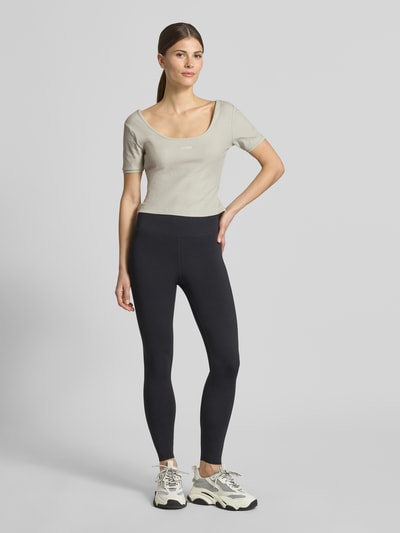 Kobiece modelka nosi Cropped T-Shirt aus Lyocell-Mix Modell 'Circe' od Guess Activewear, jasnoszary kolor, logo-stitching, krój slim fit, okrągły dekolt, elastyczna mieszanka lyocellu z bawełną, długość pleców w rozmiarze S: 31 cm, widok całej sylwetki z przodu.