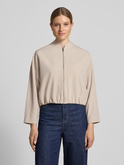 Modelka kobieca nosi Blouson mit Brustleistentasche Modell 'Jamassi' od OPUS, beżowy, materiał mix z wiskozą, krój loose fit, zapięcie na zamek, stójka, kieszeń na piersi, szerokość w rozmiarze 36: 62 cm, długość tyłu 53 cm, szerokość ramion 59 cm, długość rękawa 44 cm, faktura gładka, widok całej sylwetki z przodu.