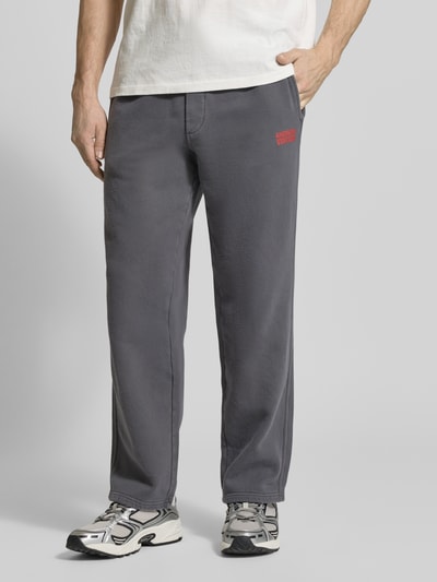 Männermodel trägt Sweatpants aus Baumwolle Modell 'PLIZZY' von American Vintage in Grau, gerader Schnitt, Label-Detail, Nahaufnahme Unterkörper.