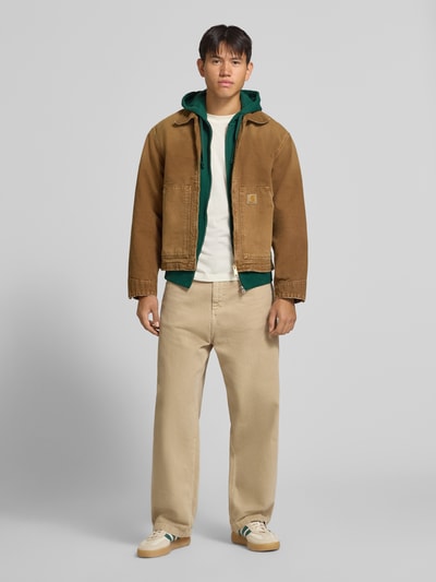 Männermodel trägt Regular Fit Sweatjacke aus Baumwoll-Mix mit Label-Detail von Superdry, beige Farbtöne, Känguru-Tasche, elastische Abschlüsse, Ganzkörperansicht von vorne.