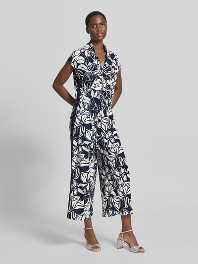 Frauenmodel trägt Jumpsuit mit Schalkragen und Kappärmeln von Betty Barclay, Material-Mix mit Stretch-Anteil, Taillierter Schnitt, Dunkelblau mit weißem floralem Muster, glatte Textur, Ganzkörperansicht von vorne.