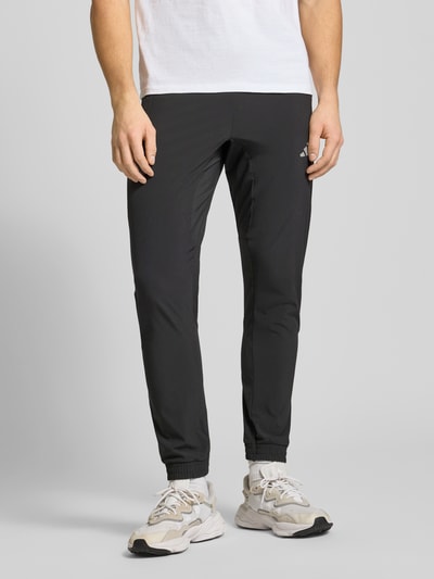 Männermodel trägt Regular Fit Trackpants mit elastischem Logo-Bund von adidas Training, unifarbenes Design, Nahaufnahme Unterkörper.