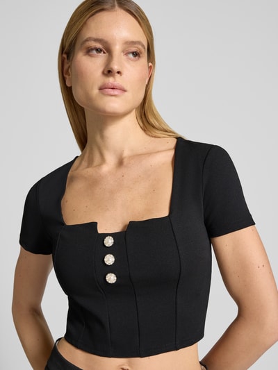 Vrouwenmodel draagt Cropped T-Shirt met Ziersteinbesatz Modell 'Evelina' van Guess, zwart, slim fit, elastische materiaalmix, cropped fit, detailaufnahme bovenlichaam.