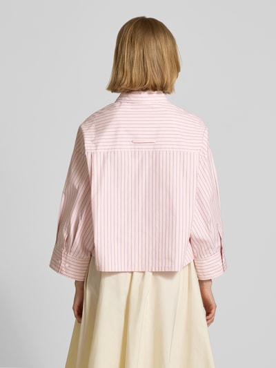 Frauenmodel trägt Boxy Fit Hemdbluse aus reiner Baumwolle Modell 'VELOCE' von MAX&Co. mit rosa-weißen Streifenmuster und weiter Manschette, Rückenpasse mit Locker Loop, Ganzkörperansicht Rückansicht.