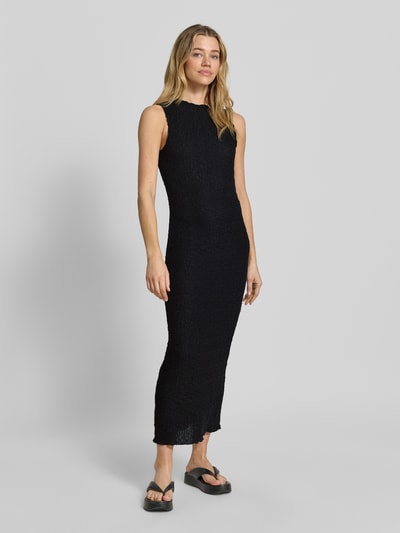 Modelka kobieca ma na sobie Maxikleid mit Rundhalsausschnitt Modell 'FALL' od Vila, czarny materiał z fakturą, proste linie, domieszka stretchu, długość tyłu w rozmiarze S: 136 cm, szerokość w rozmiarze S: 33 cm, widok całej sylwetki z przodu.