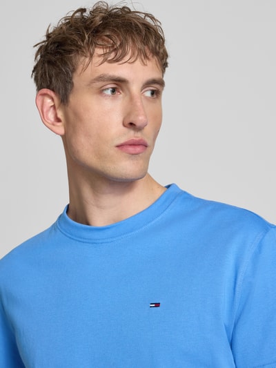 Männermodel trägt Regular Fit T-Shirt aus reiner Baumwolle von Tommy Jeans in Uni-Blau mit Logo-Stitching, Nahaufnahme Oberkörper.