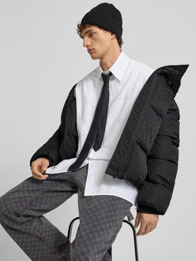Männermodel trägt schwarze Steppjacke mit Kapuze von DAILY PAPER, auffälliges Steppmuster, Regular Fit, Nahaufnahme Oberkörper.