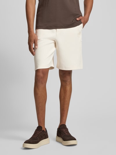 Męskimodel nosi szorty z wpuszczanymi kieszeniami model 'Joseignacio' od JOOP! Collection, mieszanka bawełny z dodatkiem streczu, krój loose fit, elastyczny pas z trokiem, naszywka z logo, szerokość w rozmiarze M: 42 cm, długość wewnętrzna nogawki w rozmiarze M: 22 cm, widok z przodu, ujęcie od pasa w dół.