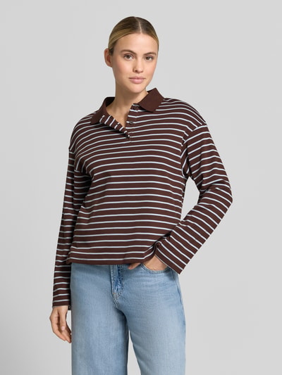 Frauenmodel trägt Relaxed Fit Poloshirt aus reiner Baumwolle Modell 'TIMOTHEE' von MANGO, braun mit weißen Streifen, Polokragen, langärmelig, glatte Struktur, Rückenlänge bei Größe S 60 cm, Ganzkörperansicht von vorne.