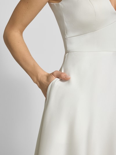 Frauenmodel trägt Brautkleid aus Satin mit V-Ausschnitt von Jake*s Cocktail, A-Linie, Midikleid, Spaghettiträger, Rückseitiger Reißverschluss, cremefarben, glatte Satin-Haptik, Ganzkörperansicht von vorne
