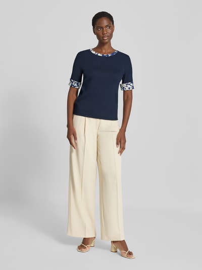 Frauenmodel trägt T-Shirt mit Rundhalsausschnitt und Ärmeln mit Aufschlag von Marc Cain, dunkelblau, Slim Fit, Baumwoll-Elasthan-Mix, Label-Detail, kombiniert mit heller Hose, Rückenlänge bei Größe 36: 54 cm, Ganzkörperansicht von vorne.