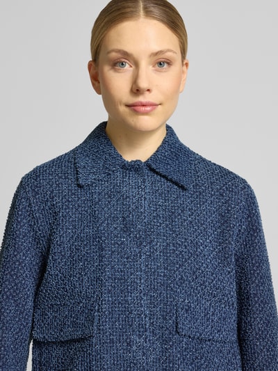 Modelka kobieca nosi żakiet 'Blazer in Bouclé-Optik mit verdecktem Verschluss' od Jake*s Collection z niebieskiej bawełny, prosty krój, imitacja bouclé, kołnierzyk typu kent, ukryte zapięcie, kieszenie z patką, długość tyłu w rozmiarze 36: 50 cm, szerokość w rozmiarze 36: 52 cm, długość rękawów w rozmiarze 36: 63 cm, zbliżenie na górną część ciała.